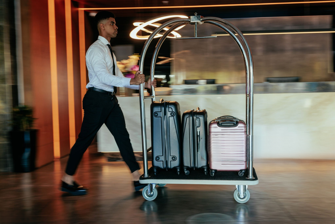 Hotel bellman pushing stainless steel luggage cart loaded with suitcases in modern lobby – Bellman Carts For Sale and service cart for hotel luggage transport.