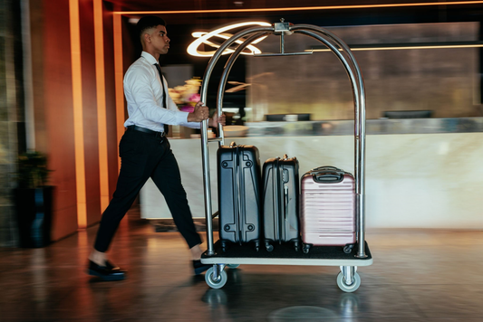 Hotel bellman pushing stainless steel luggage cart loaded with suitcases in modern lobby – Bellman Carts For Sale and service cart for hotel luggage transport.