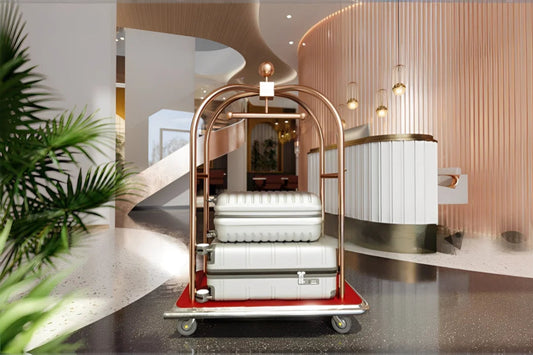 Modern hotel luggage cart with stainless steel frame and red carpet base, carrying two suitcases in a luxury lobby reception area.