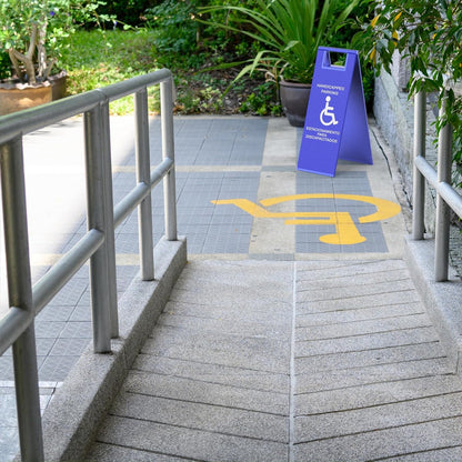 Blue ADA parking sign with wheelchair symbol marking accessible entrance ramp with painted ground markings