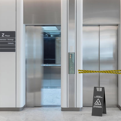 Black elevator repair sign with triangular warning positioned outside elevator doors during maintenance service