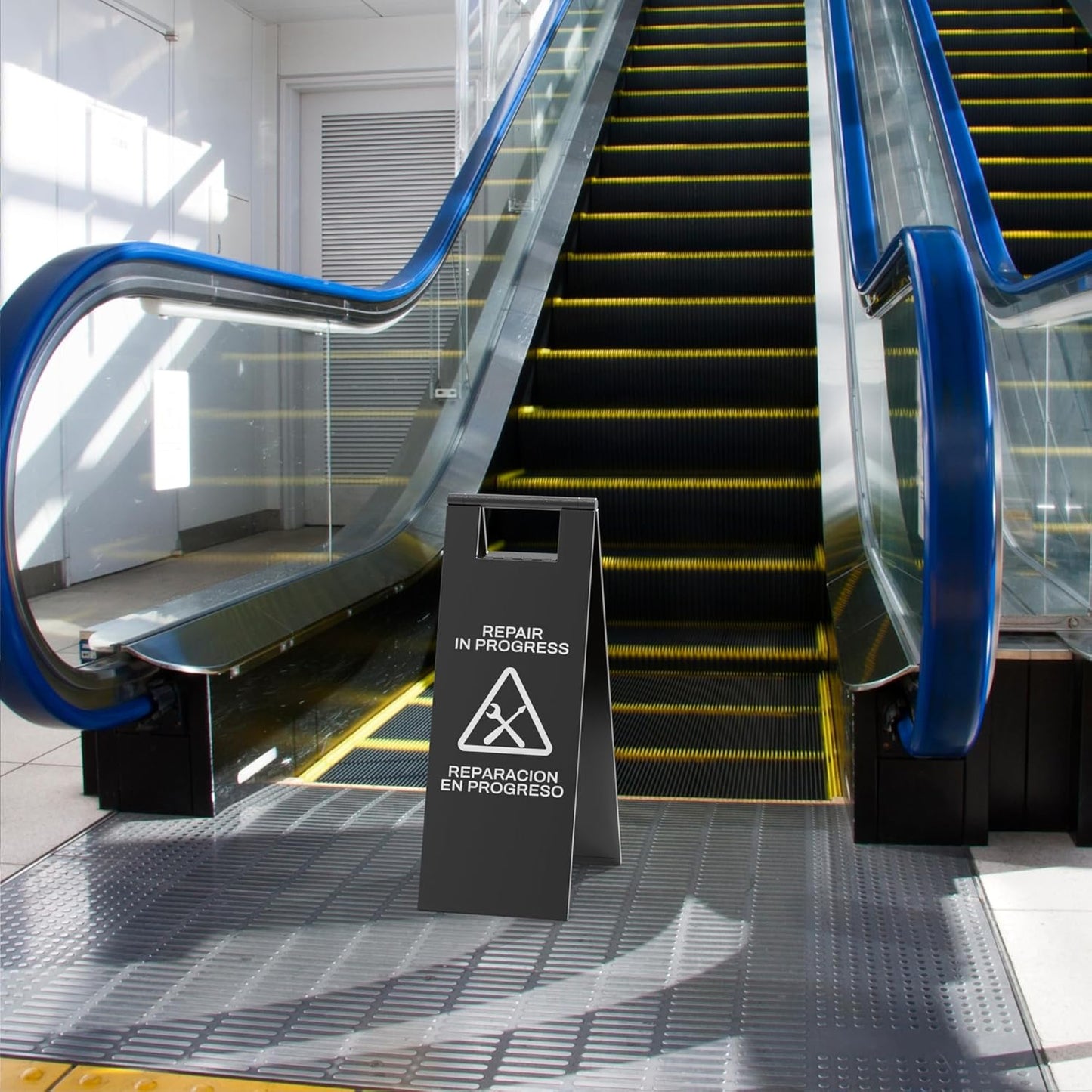 Black escalator maintenance sign with tool symbols positioned at bottom of escalator during repair work