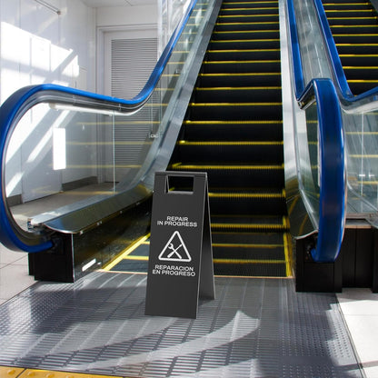 Black escalator maintenance sign with tool symbols positioned at bottom of escalator during repair work