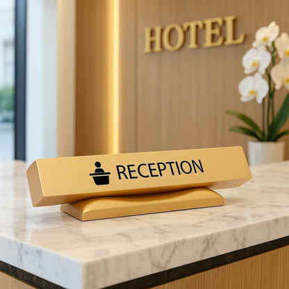 Premium gold-finished reception desk sign placed on marble hotel counter with "HOTEL" signage and white orchids in background