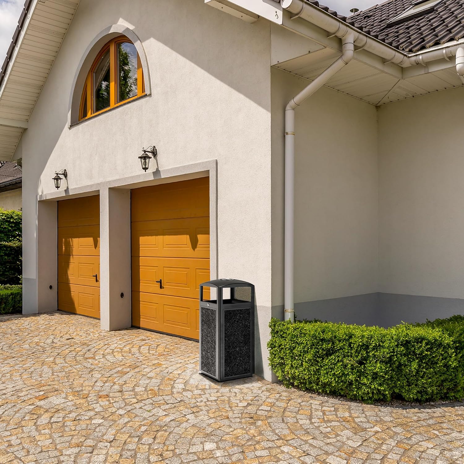 Professional outdoor waste container with stone aggregate finish positioned near residential garage entrance on decorative paved driveway
