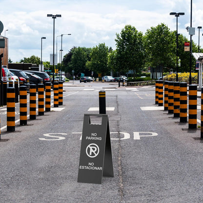 Black parking restriction sign with prohibited symbol placed in commercial parking lot with orange traffic barriers