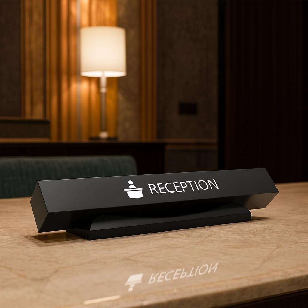 Elegant black triangular reception desk sign with white text and icon, positioned on wooden hotel reception counter with warm ambient lighting