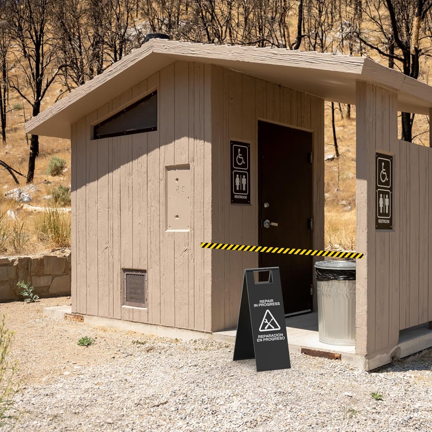 Black restroom repair sign with tool symbols blocking access to public bathroom facility during maintenance work