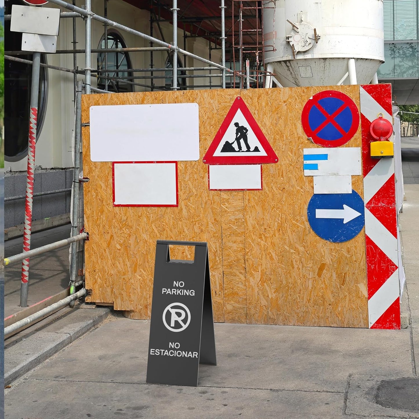 Black temporary no parking sign with prohibited symbol positioned at construction site with safety barriers and traffic signs