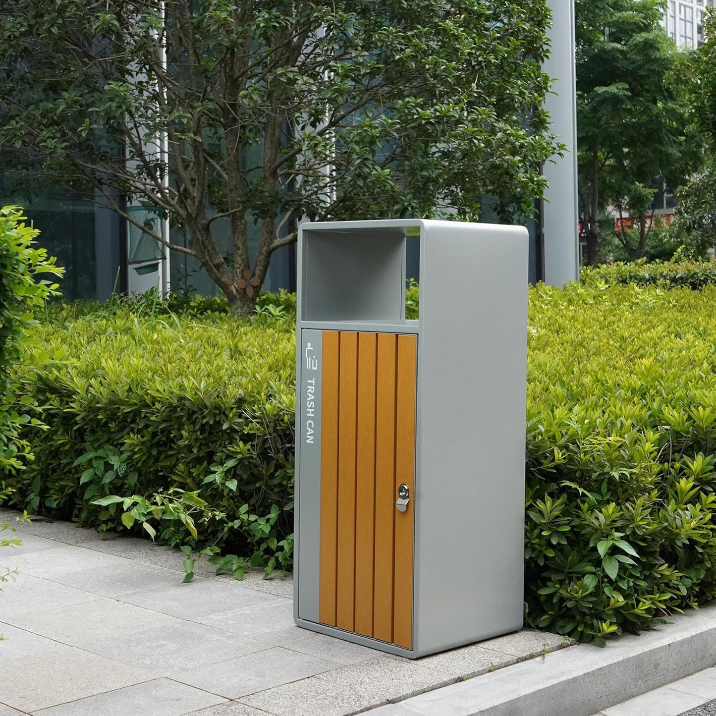 Modern outdoor trash can with wood-panel door integrated into urban landscape setting with green plants and city buildings