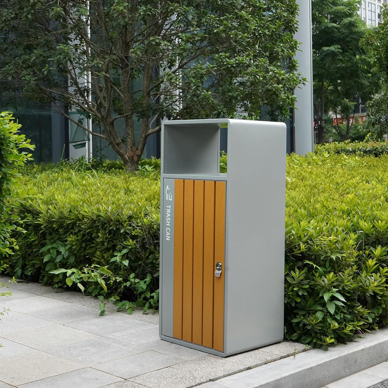 Modern outdoor trash can with wood-panel door integrated into urban landscape setting with green plants and city buildings