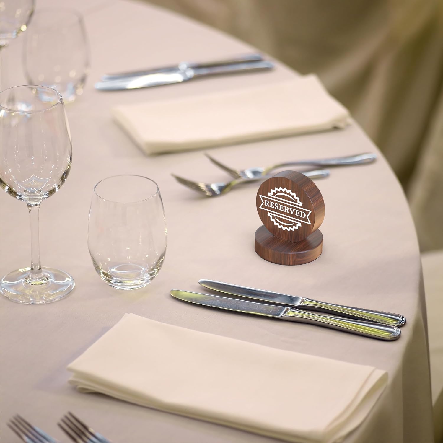 Dark wood reserved sign on white tablecloth with crystal stemware and silver cutlery arrangement