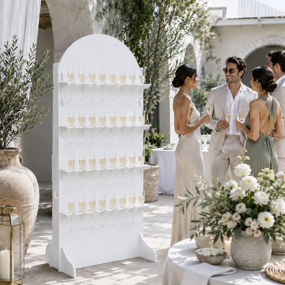 Guests gathered beside a freestanding white 32-flute champagne wall with floral reception decor